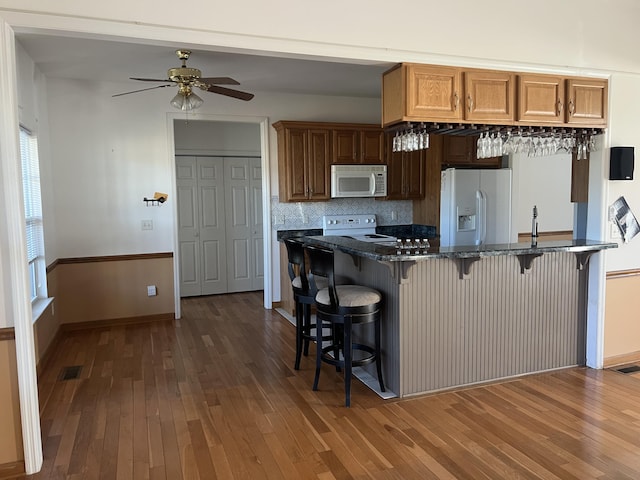 kitchen with white appliances, visible vents, dark wood-style floors, tasteful backsplash, and a kitchen bar