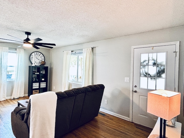 living area with visible vents, a textured ceiling, baseboards, and wood finished floors