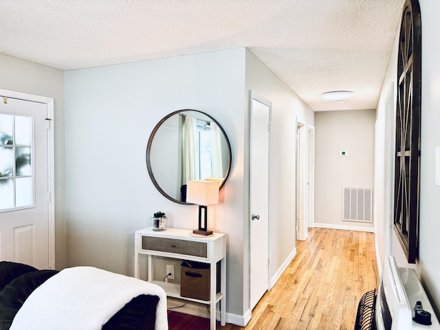 bedroom with a textured ceiling, light wood-style flooring, visible vents, and baseboards