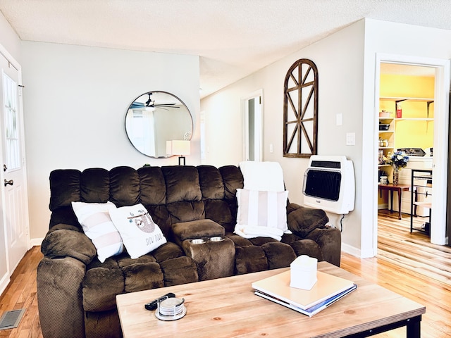 living room featuring light wood finished floors, heating unit, visible vents, a textured ceiling, and baseboards