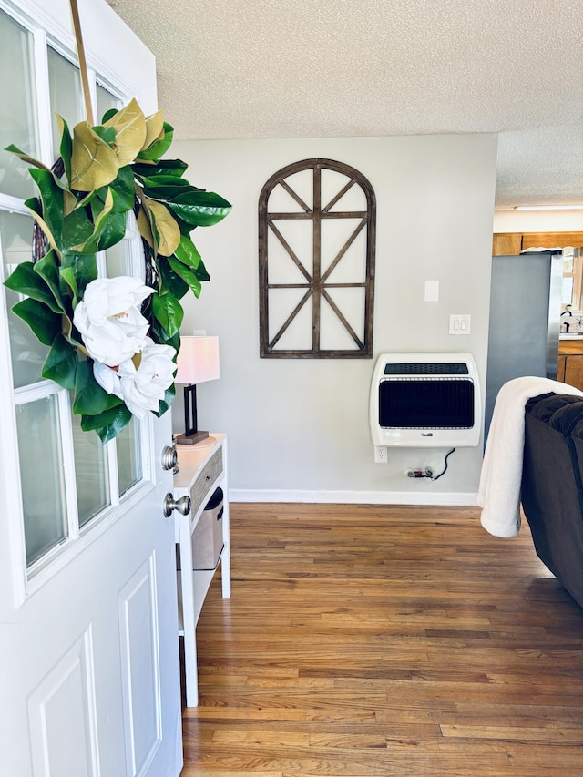 interior details featuring baseboards, a textured ceiling, heating unit, and wood finished floors