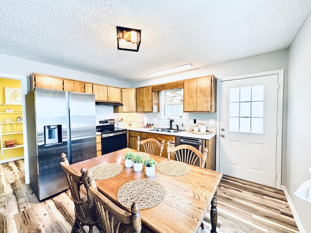 kitchen with stainless steel appliances, light countertops, a sink, light wood-type flooring, and under cabinet range hood