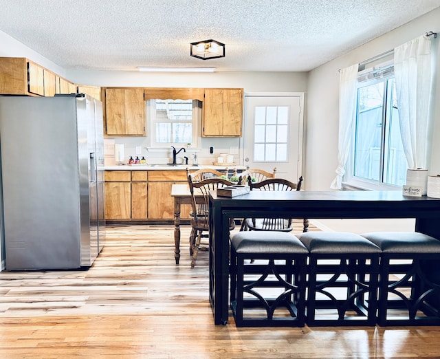 kitchen featuring light countertops, a sink, a textured ceiling, light wood-type flooring, and stainless steel fridge