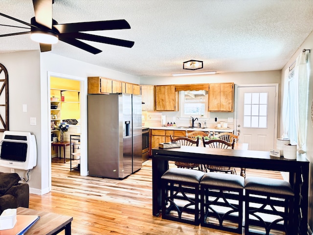 kitchen with a sink, light wood-style floors, light countertops, stainless steel refrigerator with ice dispenser, and heating unit