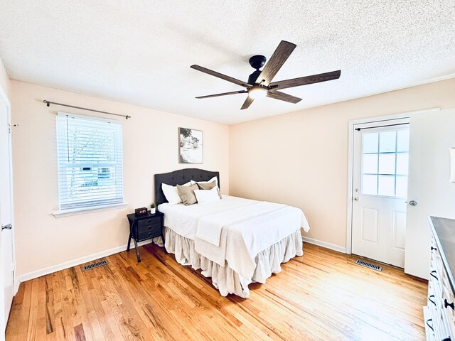 bedroom with light wood finished floors, baseboards, visible vents, and a textured ceiling