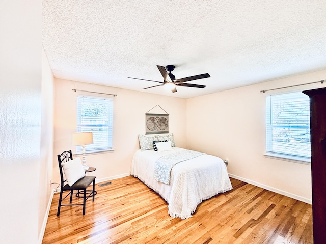 bedroom featuring a textured ceiling, wood finished floors, a ceiling fan, visible vents, and baseboards