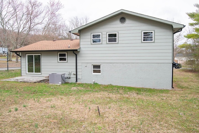 back of house with a shingled roof, central AC, a yard, and stucco siding