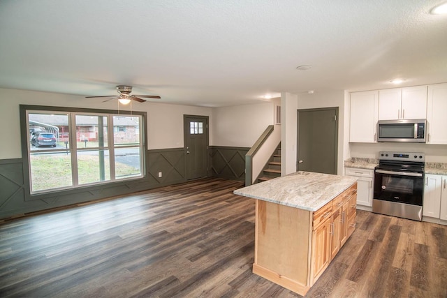 kitchen featuring light stone counters, stainless steel appliances, dark wood-type flooring, a kitchen island, and wainscoting