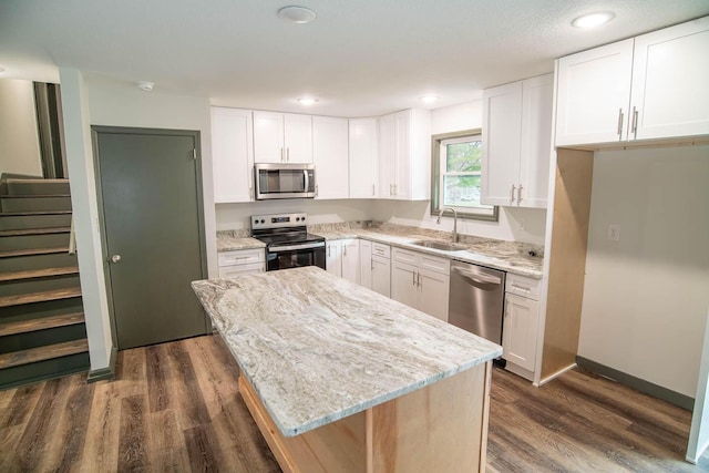 kitchen featuring dark wood-type flooring, a center island, light stone countertops, stainless steel appliances, and a sink