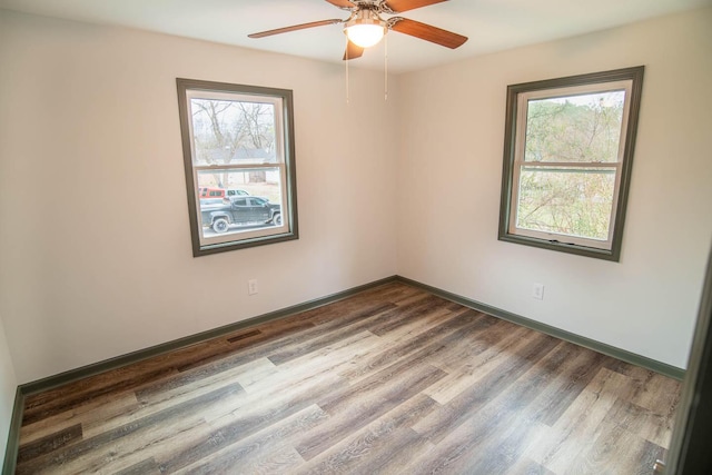 spare room with visible vents, wood finished floors, a wealth of natural light, and baseboards