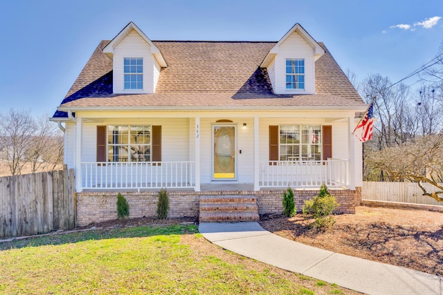 cape cod house featuring a porch, a front yard, fence, and a shingled roof