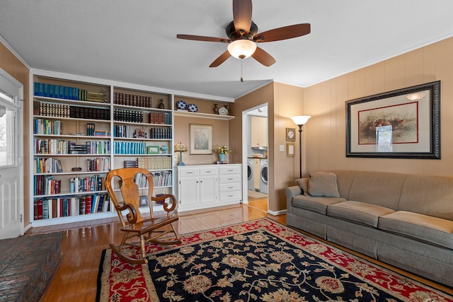 living area featuring built in features, washer and clothes dryer, a ceiling fan, ornamental molding, and light wood-type flooring