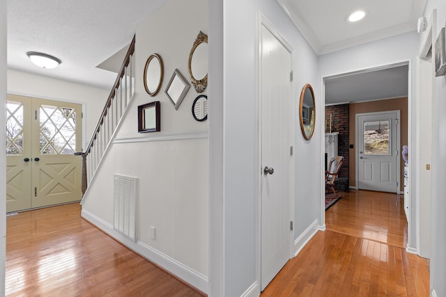 foyer featuring visible vents, french doors, stairway, light wood-type flooring, and crown molding