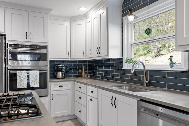 kitchen with appliances with stainless steel finishes, backsplash, a sink, and white cabinetry