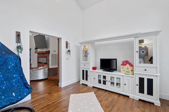 living room with a glass covered fireplace, wood finished floors, a high ceiling, and baseboards