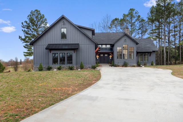 modern farmhouse style home with a shingled roof, concrete driveway, a front lawn, a standing seam roof, and a chimney