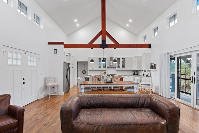 living area featuring french doors, light wood finished floors, high vaulted ceiling, and baseboards