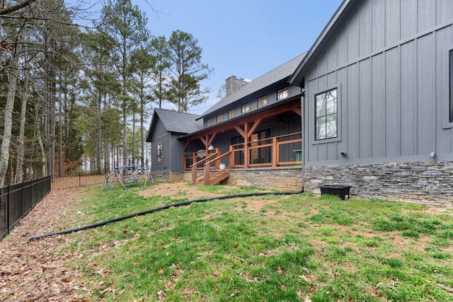 back of house with a yard, a chimney, board and batten siding, fence, and stone siding