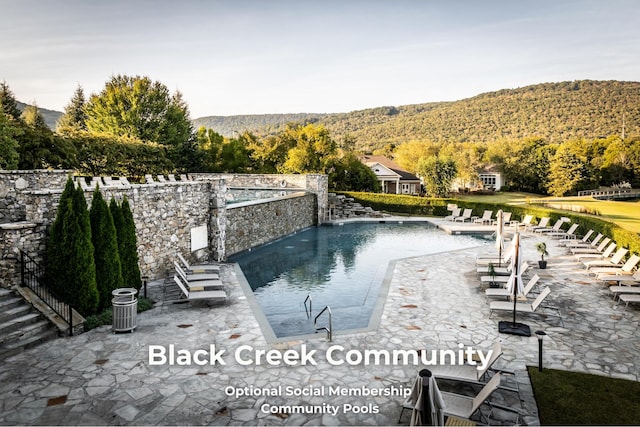 community pool with a forest view, a mountain view, and a patio