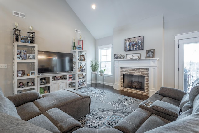 living room featuring high vaulted ceiling, a fireplace, wood finished floors, and visible vents