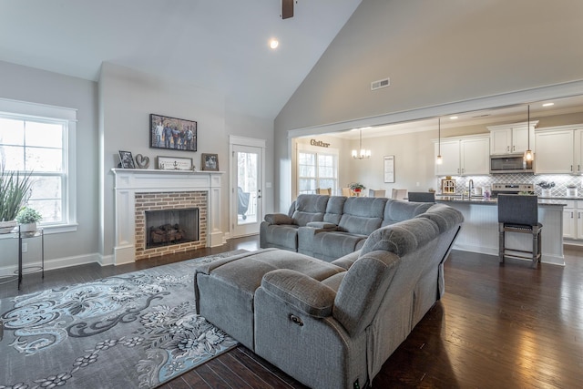 living room featuring dark wood-style flooring, visible vents, a brick fireplace, high vaulted ceiling, and baseboards