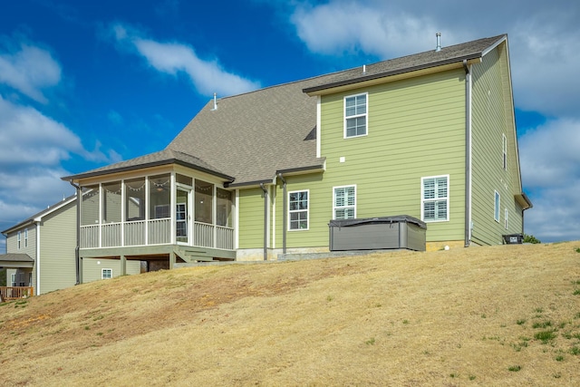 back of property with a sunroom, roof with shingles, and a hot tub