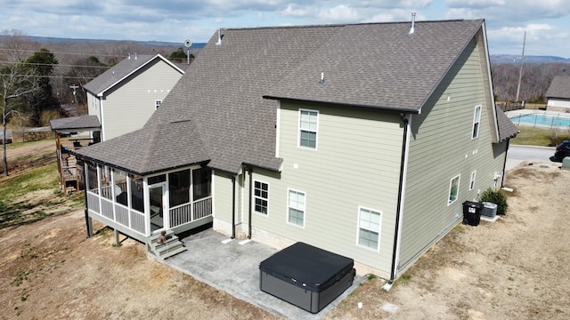 rear view of property with a patio, central air condition unit, a sunroom, driveway, and roof with shingles