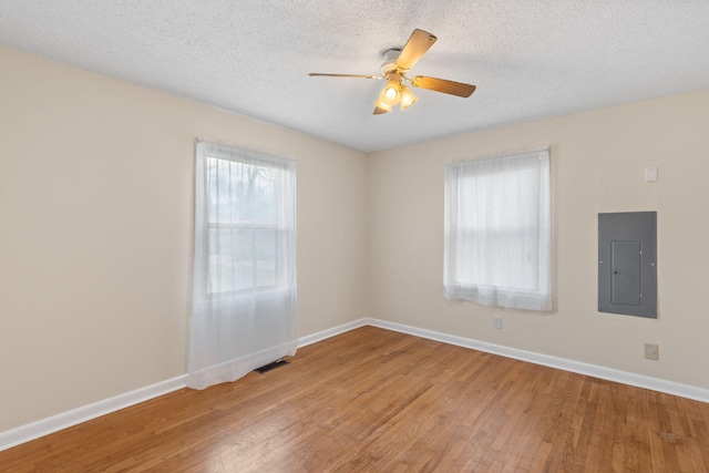 unfurnished room with electric panel, visible vents, light wood finished floors, and baseboards