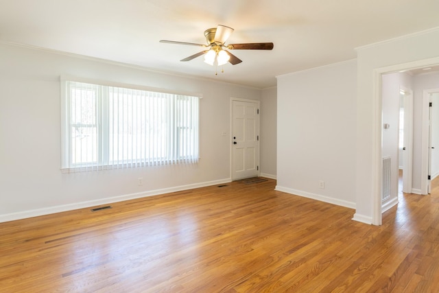 spare room with light wood finished floors, baseboards, visible vents, and crown molding