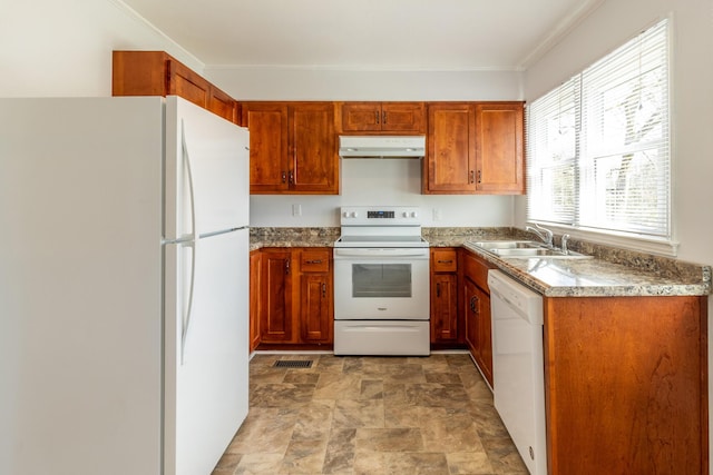 kitchen with under cabinet range hood, white appliances, a sink, stone finish flooring, and brown cabinetry