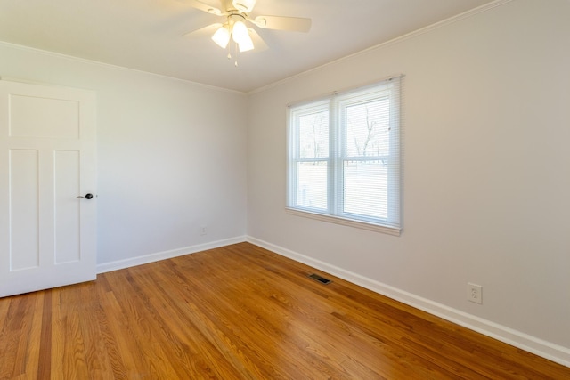 spare room featuring light wood finished floors, baseboards, visible vents, a ceiling fan, and ornamental molding