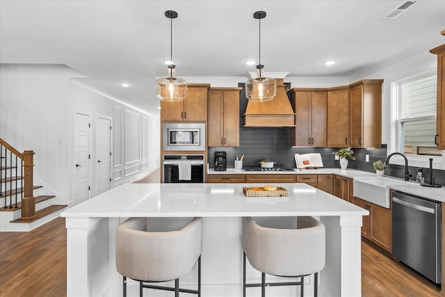 kitchen featuring custom exhaust hood, brown cabinets, stainless steel appliances, and a sink