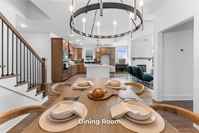 dining room with light wood finished floors, a large fireplace, baseboards, stairs, and a notable chandelier