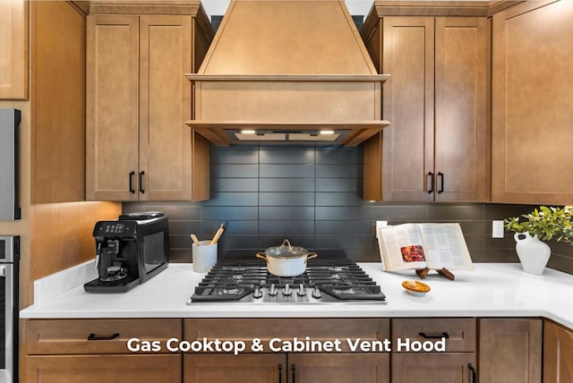 kitchen with brown cabinets, backsplash, stainless steel gas stovetop, light countertops, and custom exhaust hood