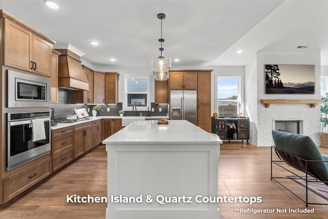 kitchen featuring a center island, decorative light fixtures, wood finished floors, custom exhaust hood, and stainless steel appliances