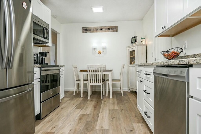 kitchen with stainless steel appliances, white cabinets, light stone countertops, light wood-type flooring, and baseboards