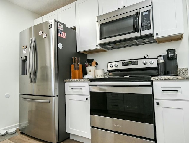 kitchen featuring appliances with stainless steel finishes, white cabinets, light stone counters, and wood finished floors