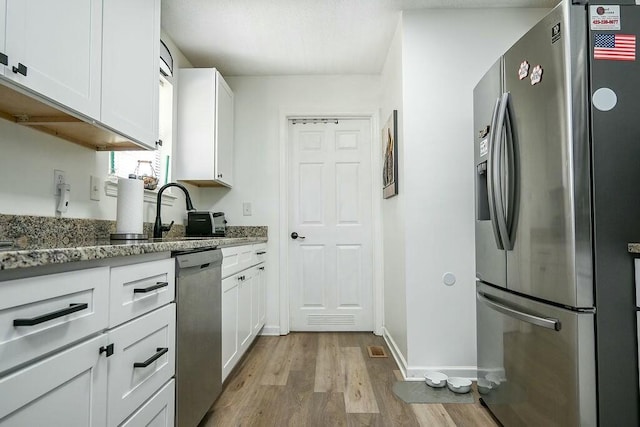 kitchen with light stone countertops, light wood-style floors, white cabinetry, and appliances with stainless steel finishes