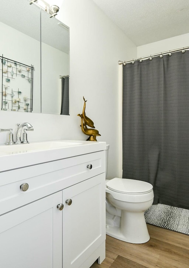 full bath featuring toilet, wood finished floors, curtained shower, a textured ceiling, and vanity