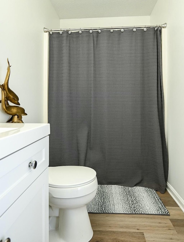 bathroom featuring toilet, a shower with shower curtain, wood finished floors, and vanity