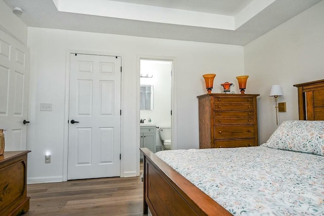 bedroom with a raised ceiling, ensuite bath, baseboards, and wood finished floors