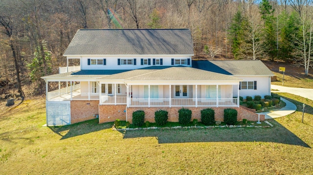 country-style home featuring covered porch, a wooded view, and a front lawn