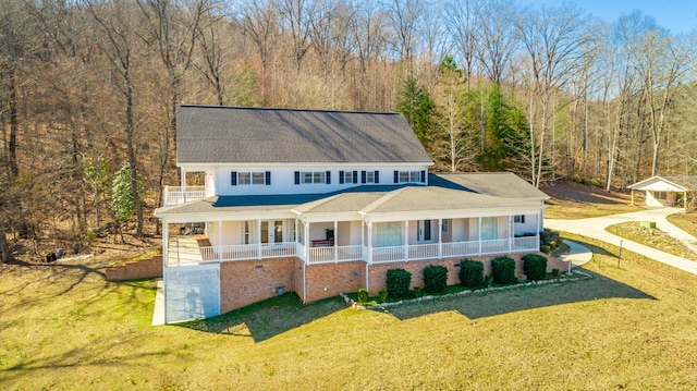 view of front of house featuring a porch, a front lawn, and a wooded view