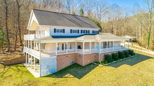 view of front of property featuring a view of trees, a balcony, roof with shingles, covered porch, and a front yard