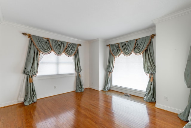 spare room featuring ornamental molding, wood-type flooring, visible vents, and baseboards