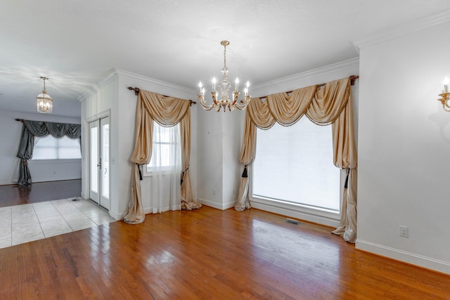 unfurnished dining area with an inviting chandelier, crown molding, baseboards, and wood finished floors