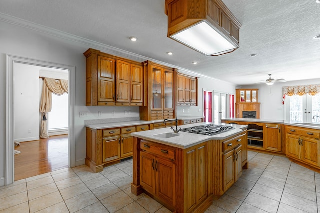 kitchen with brown cabinetry, light tile patterned flooring, a sink, and stainless steel gas stovetop