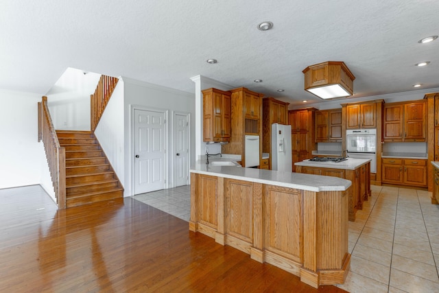 kitchen featuring white appliances, ornamental molding, brown cabinets, light countertops, and a sink