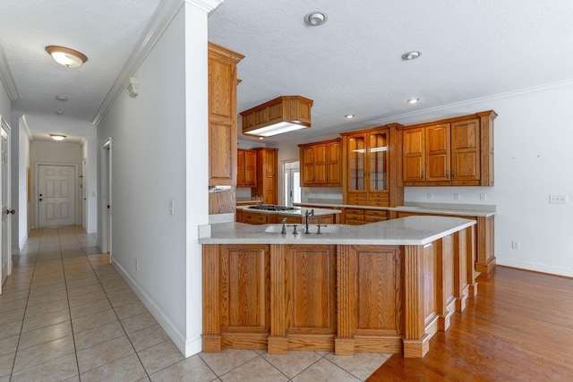 kitchen with crown molding, a peninsula, light countertops, brown cabinetry, and stainless steel gas stovetop