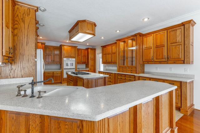 kitchen with white appliances, a sink, light countertops, ornamental molding, and brown cabinets